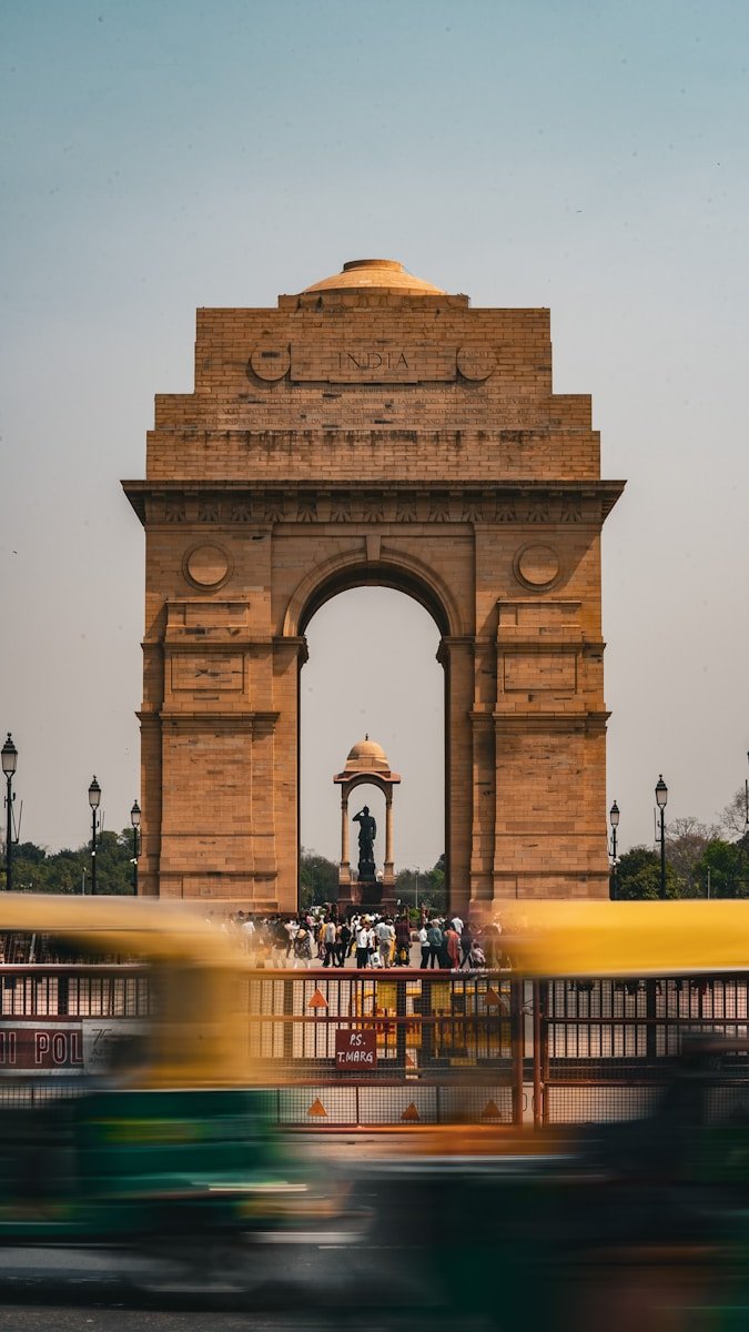a yellow bus driving past a large stone arch